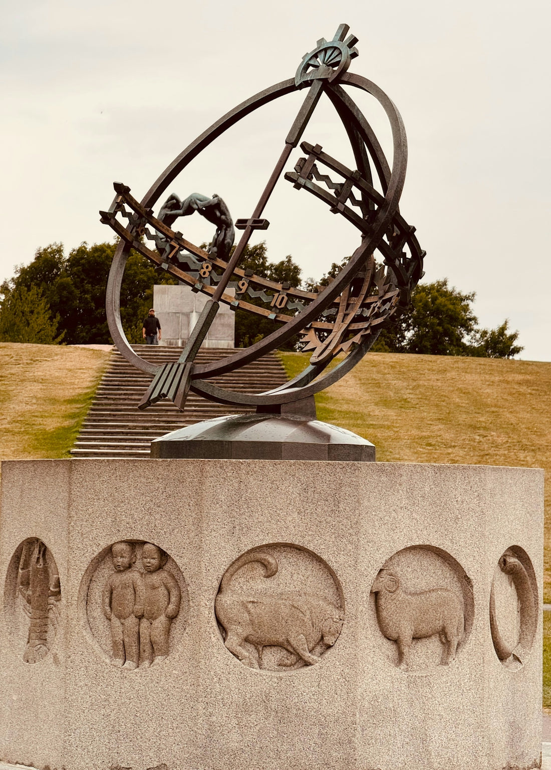 Large metal sculpture with zodiac carvings on pedestal.